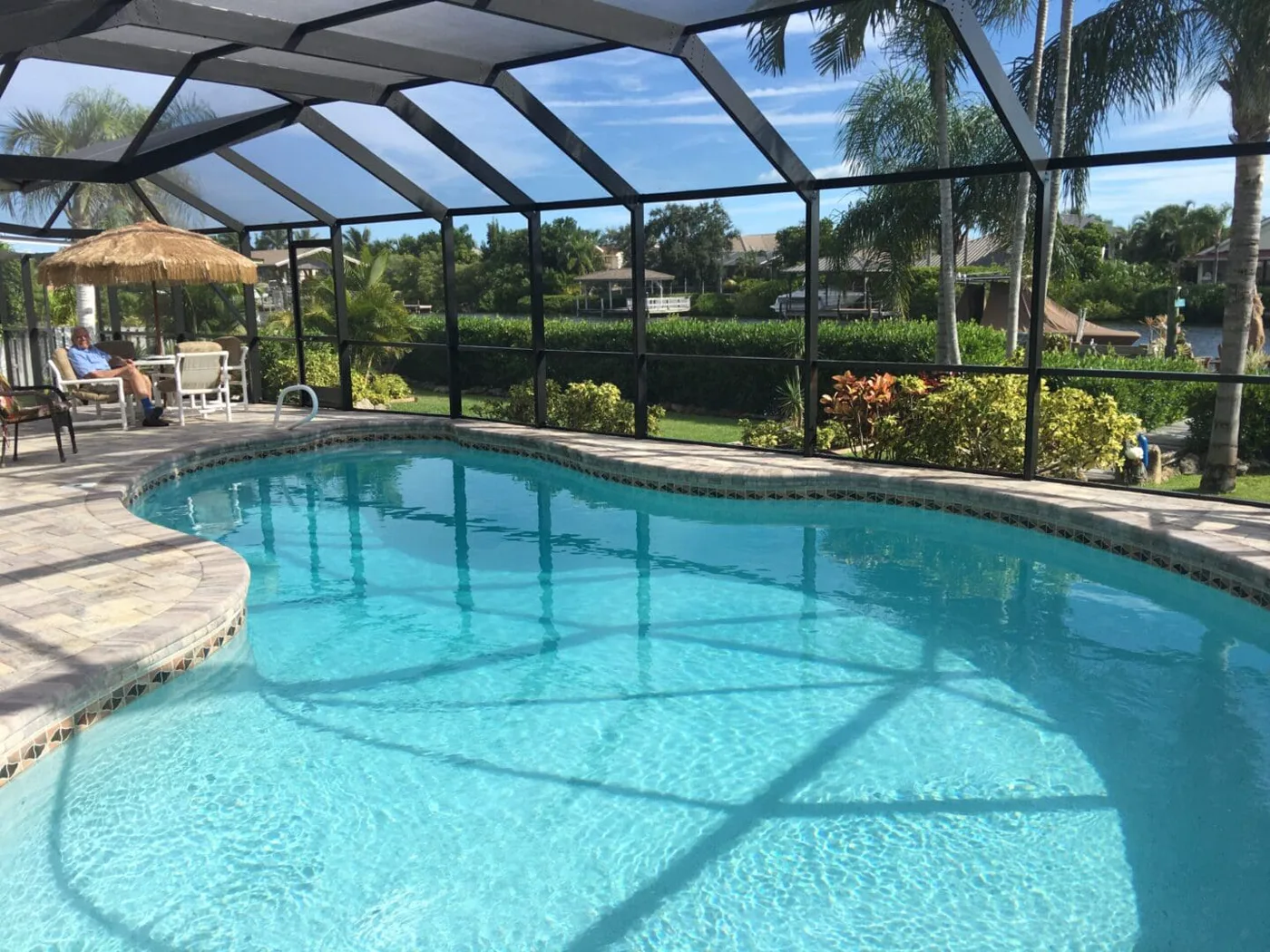 Custom Pool Design & Construction — freeform concrete pool inside a screened lanai overlooking a lake, by Pool Builder of Brevard